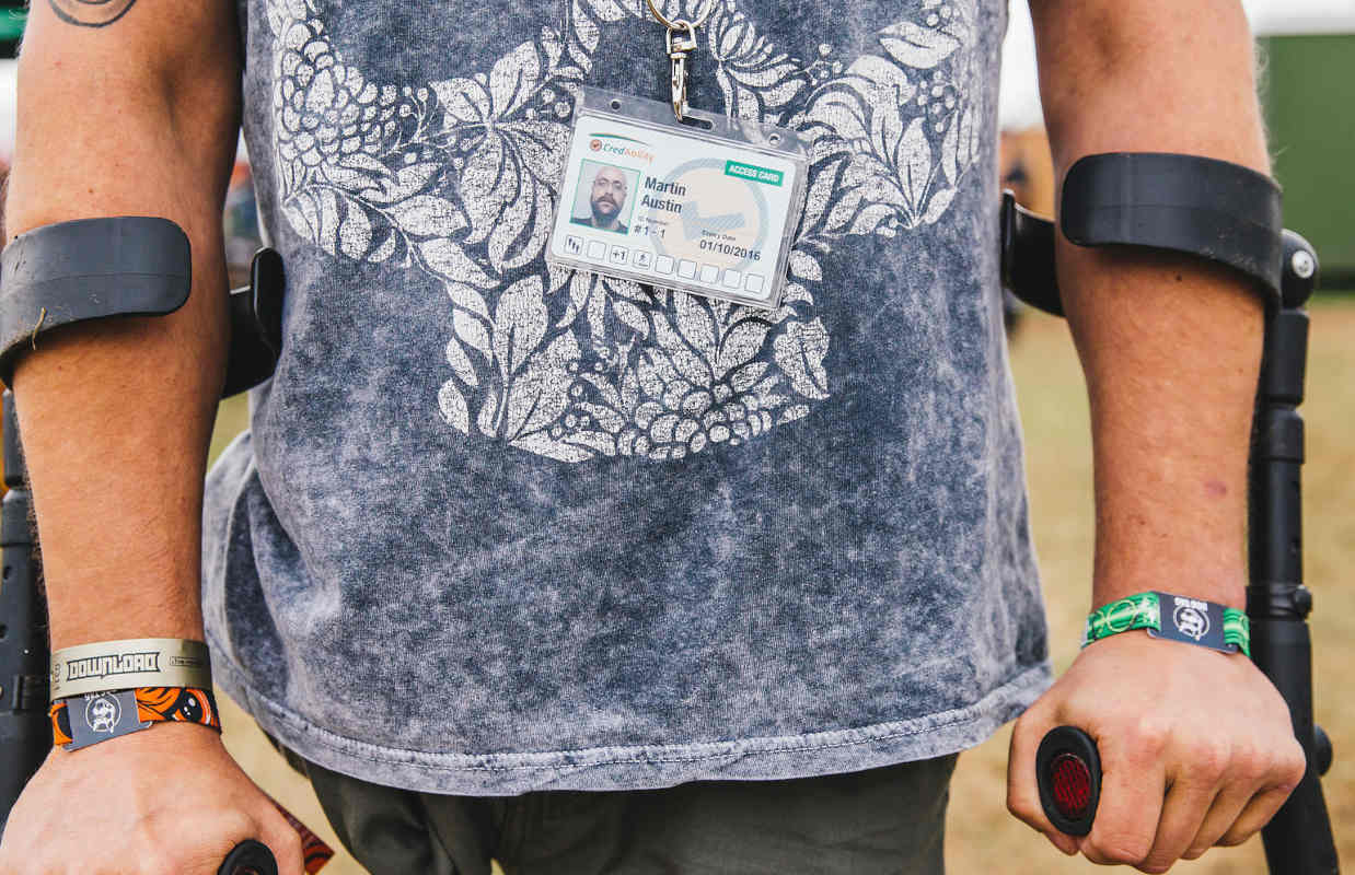 Photograph of an Access Card holder at a music festival, standing with crutches, wearing their Access Card on a lanyard around their neck